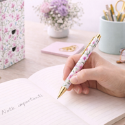 Penna a sfera con motivo floreale utilizzata per scrivere su un quaderno in un ambiente da scrivania ordinato ed elegante, ideale per l’uso quotidiano
