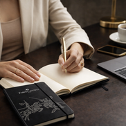 Donna elegante che scrive su un notebook A5 Faber-Castell nero su una scrivania ordinata, ideale per appunti di lavoro e uso quotidiano.